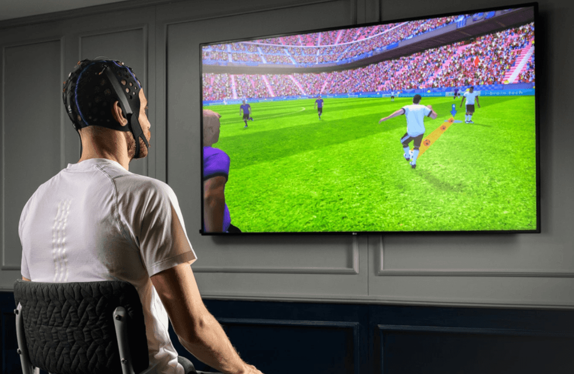 Person wearing an EEG cap watching a soccer game on a large screen.