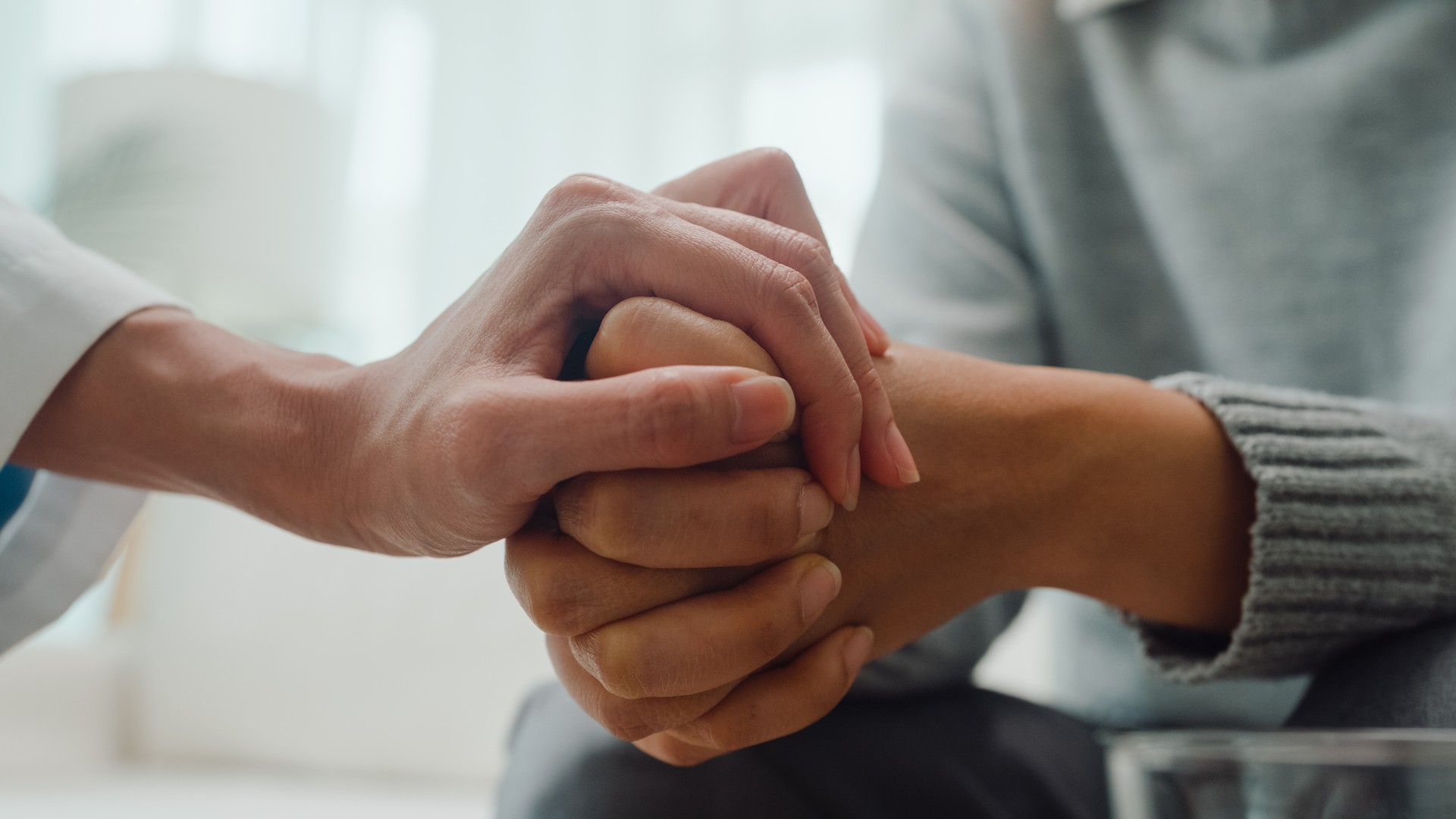 Primer plano de una joven psicoterapeuta asiática discutiendo un problema y tocando la mano joven deprimida sentada en el sofá de la clínica. Seguro médico, Salud mental.