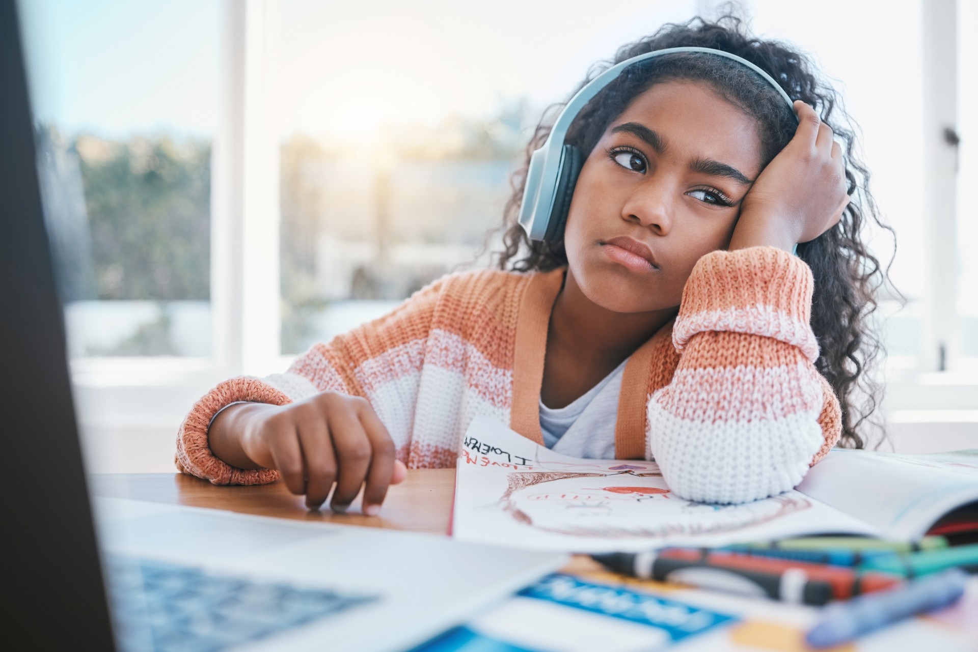 Niño, auriculares y niña cansados de la escuela en casa, el aprendizaje electrónico y la futura educación en línea. Pensando, aburrido y niño con TDAH, autismo y triste en la computadora portátil mientras dibuja y escucha audio en la mesa